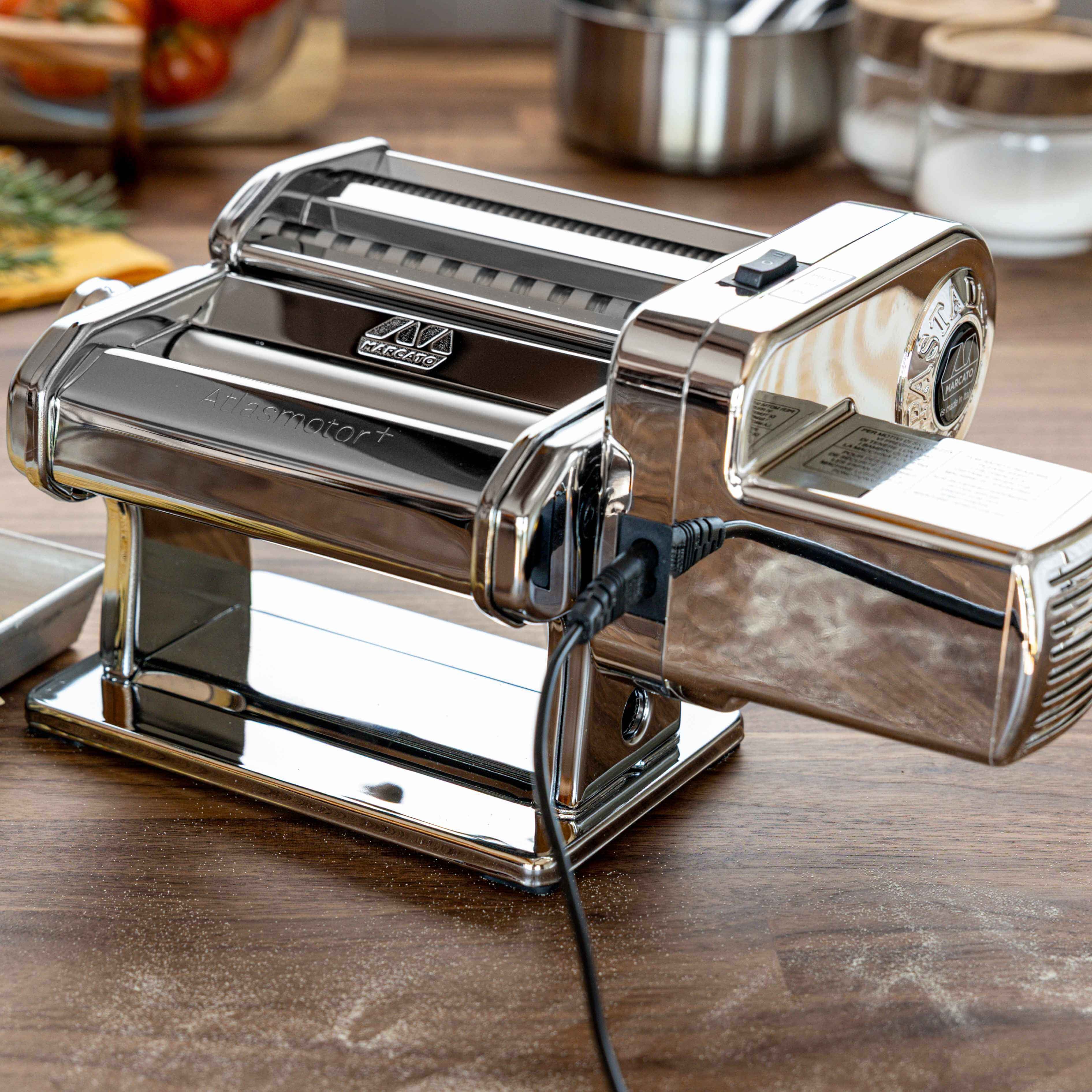 Pasta maker on a wooden table with fresh pasta and ingredients in the background
