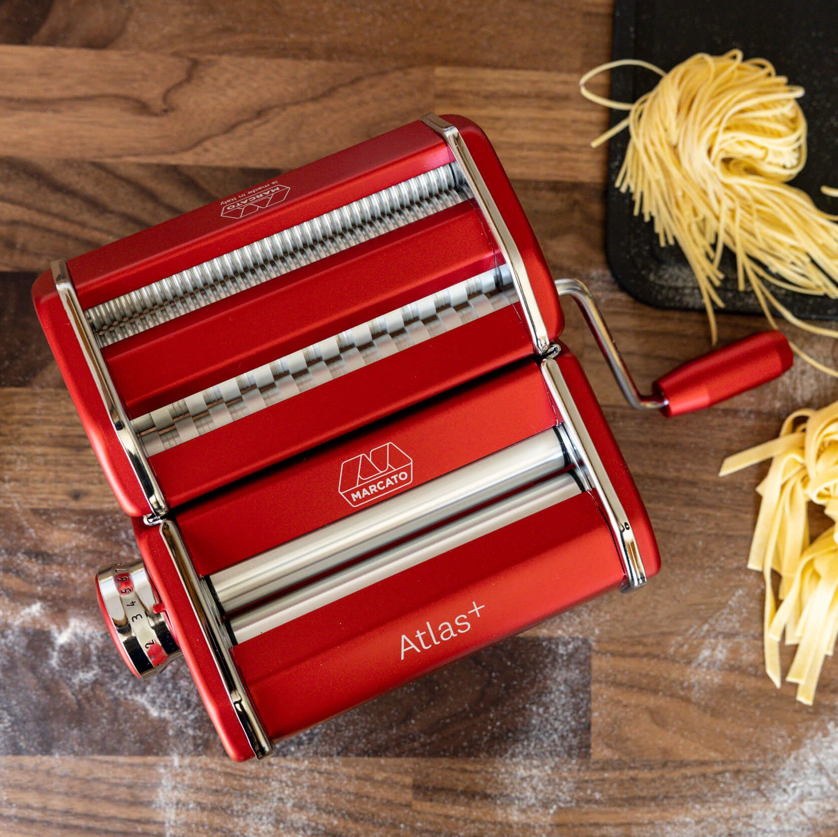 Red pasta maker with fresh pasta on a wooden surface