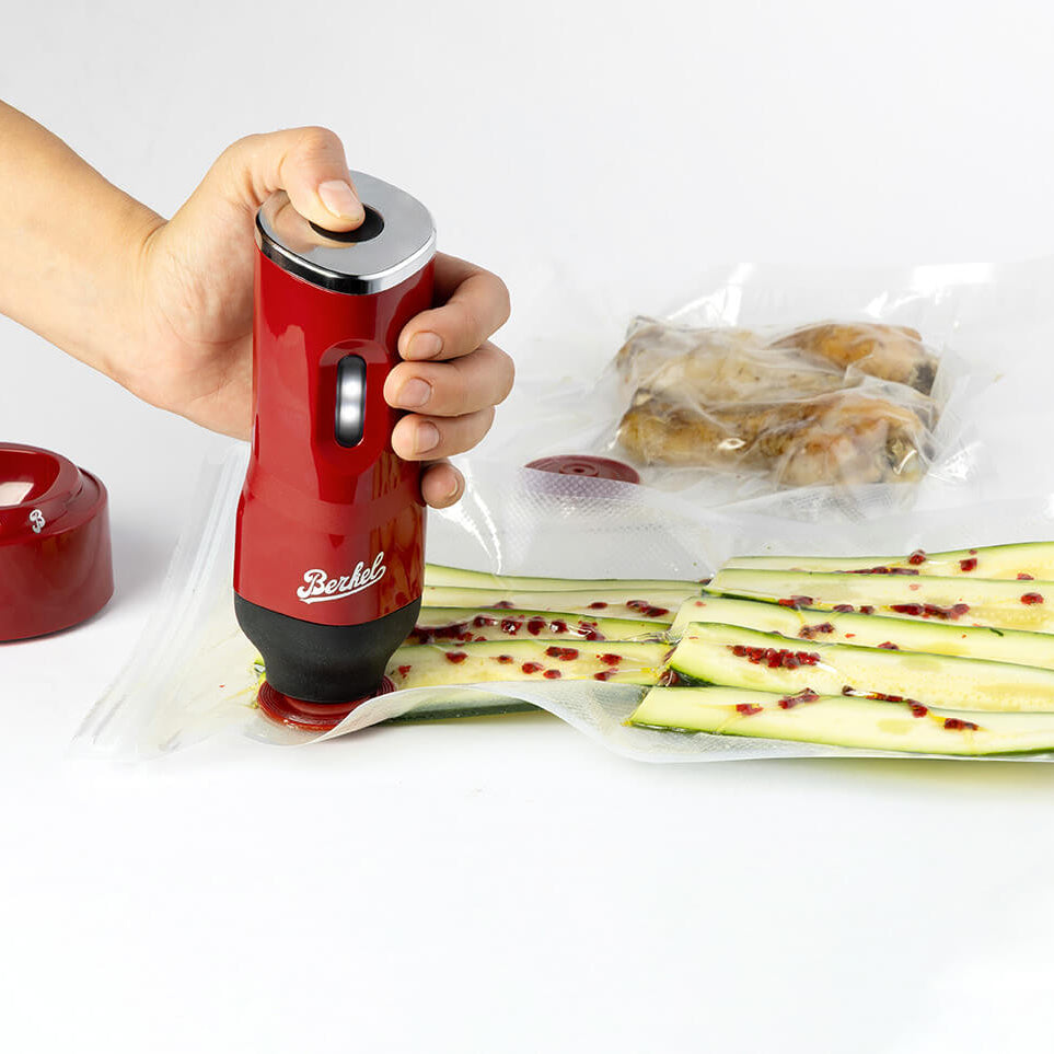 Person using a red vacuum sealer on zucchini slices with a white background