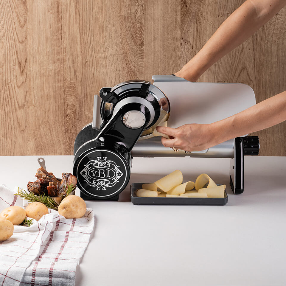 Black Berkel Icon Line 170 food slicer on a white countertop, being used to slice potatoes.